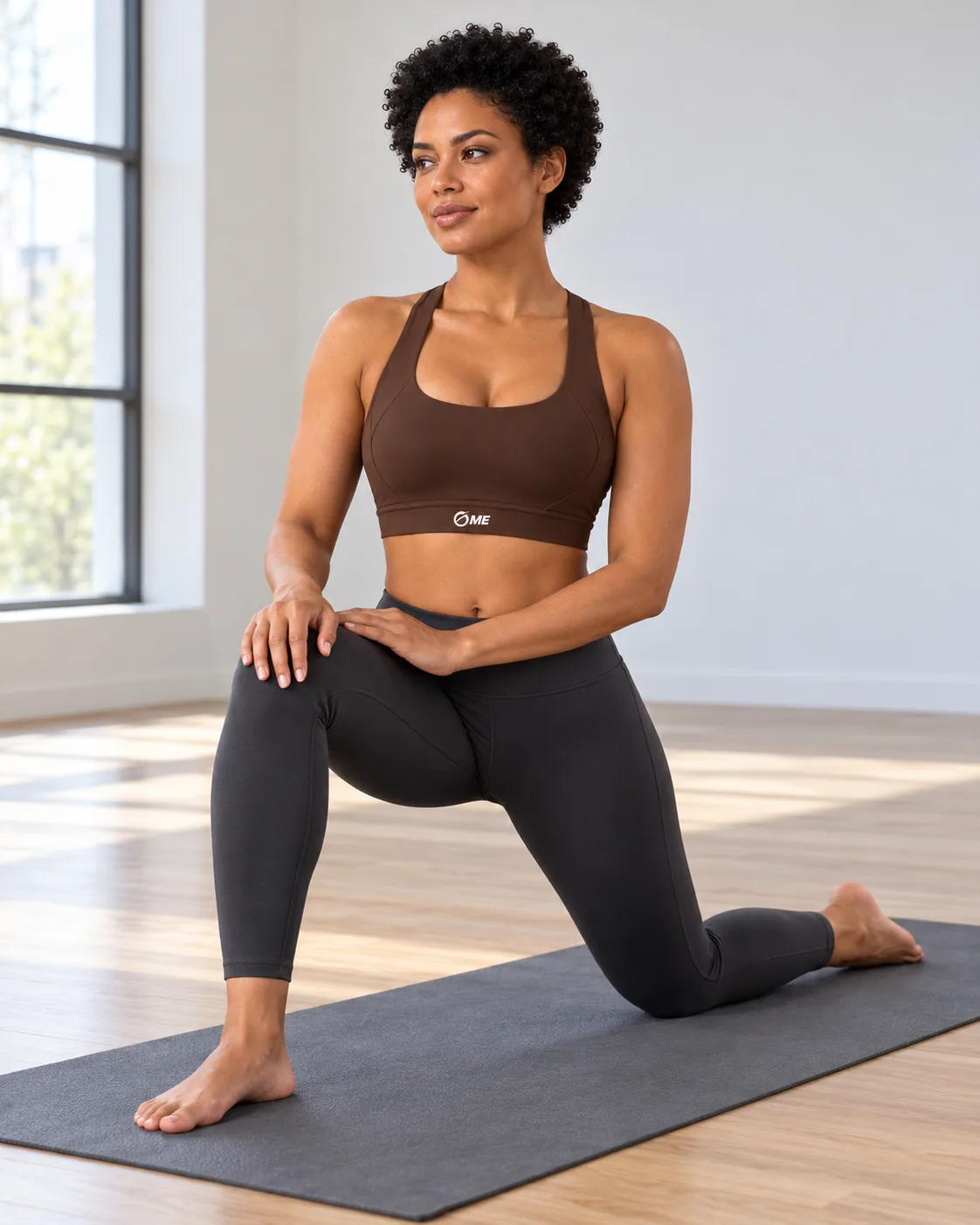 Top Fenicia Core marrón, zancada baja de yoga sobre esterilla.