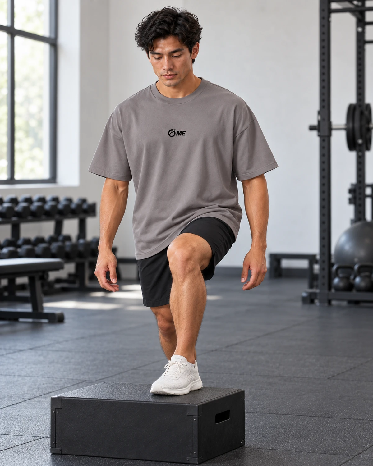 Modelo con camiseta MALAKA gris realizando un paso sobre un cajón en un gimnasio.
